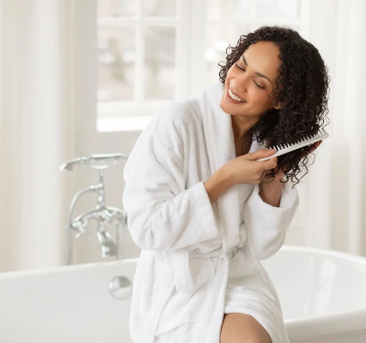 A woman in a robe smiling as she brushes through thick, healthy hair